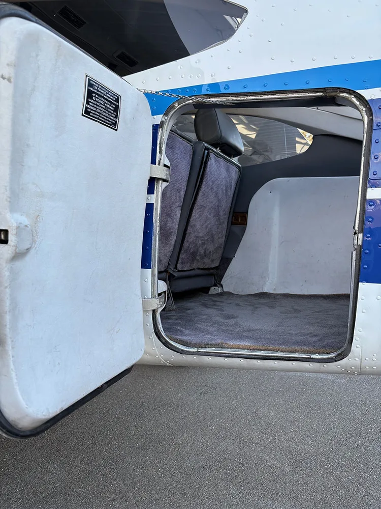 The open cargo door of a Cessna 182, showing the rear cabin seats folded down and carpeted floor.