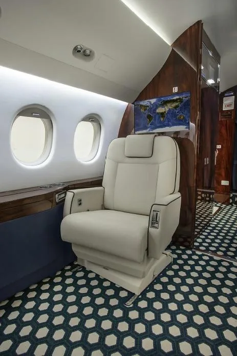 A comfortable white leather seat in the aircraft cabin with a world map displayed on a screen in the background.
