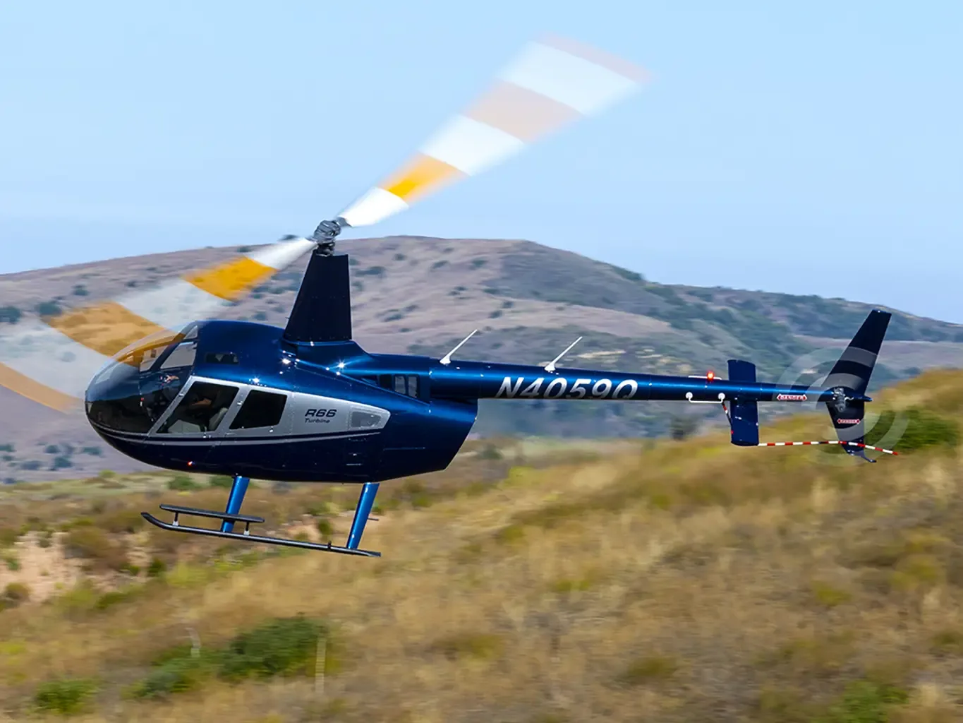 A blue Robinson R66 Turbine helicopter with registration N4059Q flies over a dry, hilly landscape.