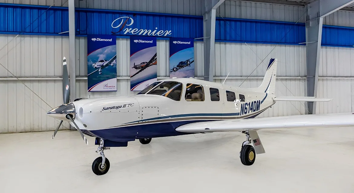 A front 3/4 view of a white and blue Piper Saratoga II TC aircraft, registration N614DM, in a hangar.