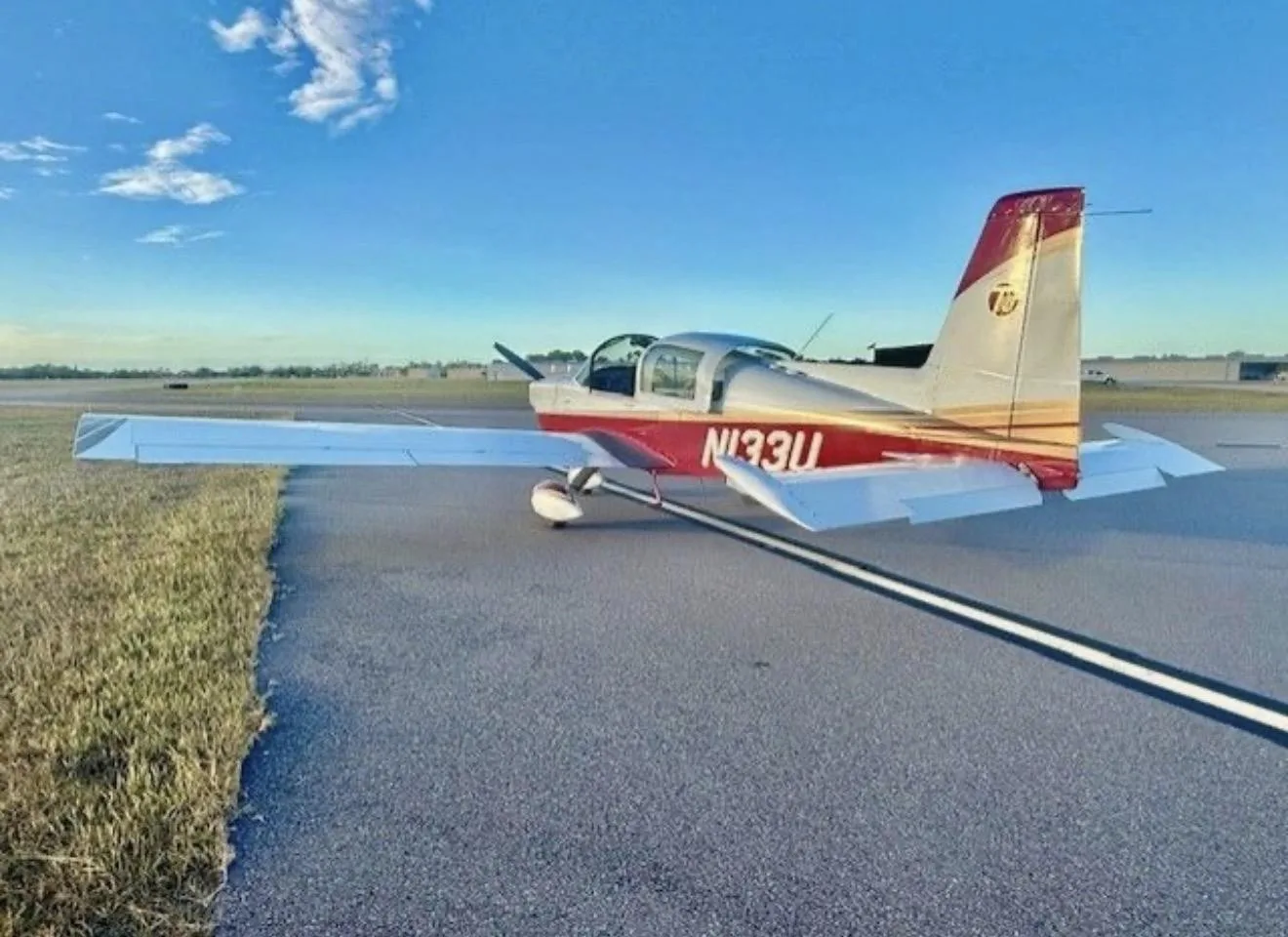 A rear three-quarter view of a white and red American General AG-5B Tiger aircraft with registration N133U on a runway.