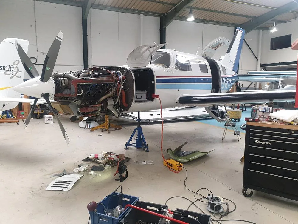 A white and blue Piper PA-46-350P Malibu Mirage aircraft, registration N9127Z, undergoing maintenance in a hangar with its engine cowling removed.
