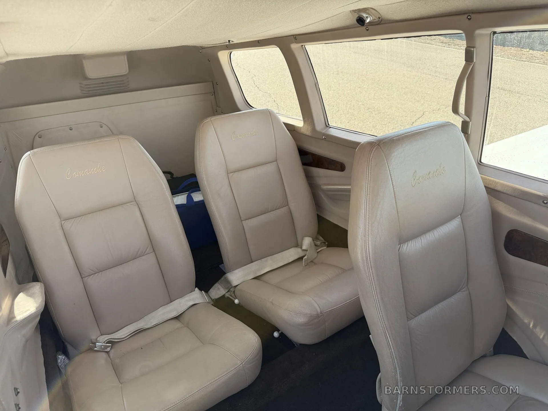 Three tan leather passenger seats are visible in the rear cabin of a small aircraft.