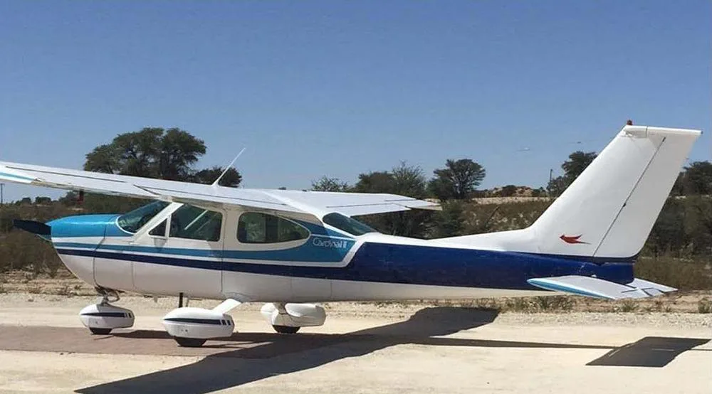 A white and blue Cessna 210 Centurion aircraft parked on a dirt airfield under a clear sky.