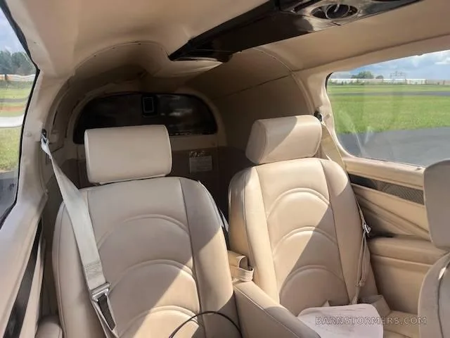 The light tan leather interior cabin of a small aircraft, showing two front seats and the rear baggage area.