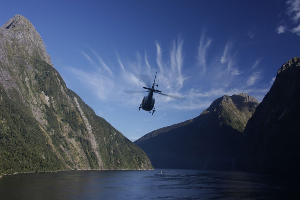 A helicopter flies between mountains over a body of water.