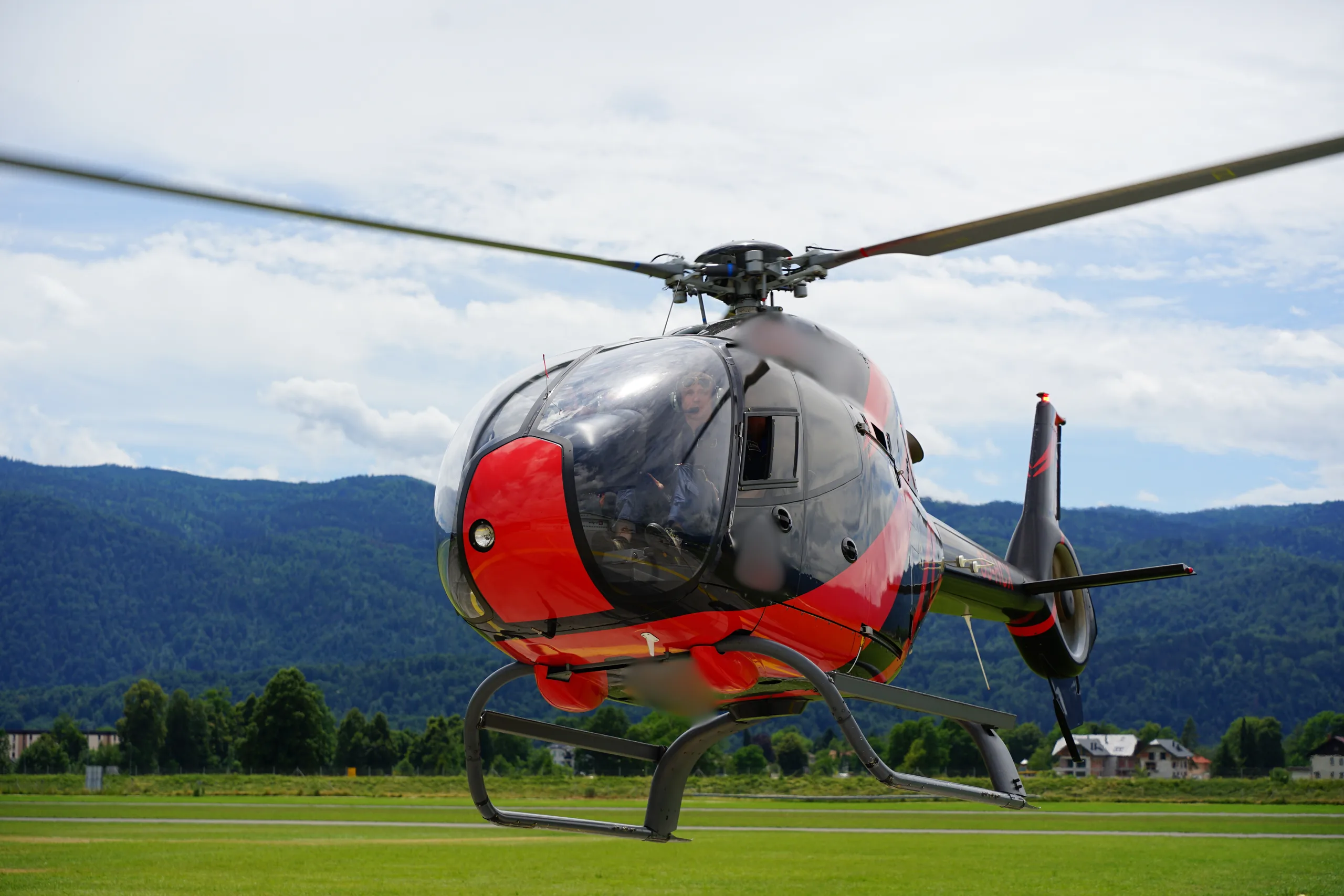 A black and red helicopter is shown from a low angle, with green hills in the background.