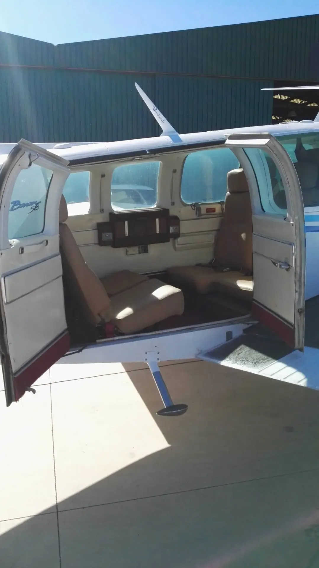 View into the cabin of a twin-engine propeller aircraft showing two rows of tan seats and an open door.