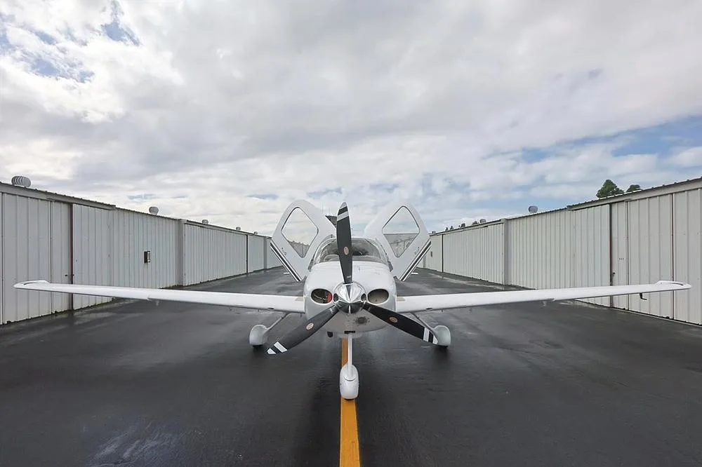 Front view of a white Cirrus SR22 aircraft with N3000D registration and both doors open, centered on a yellow line on a wet tarmac.