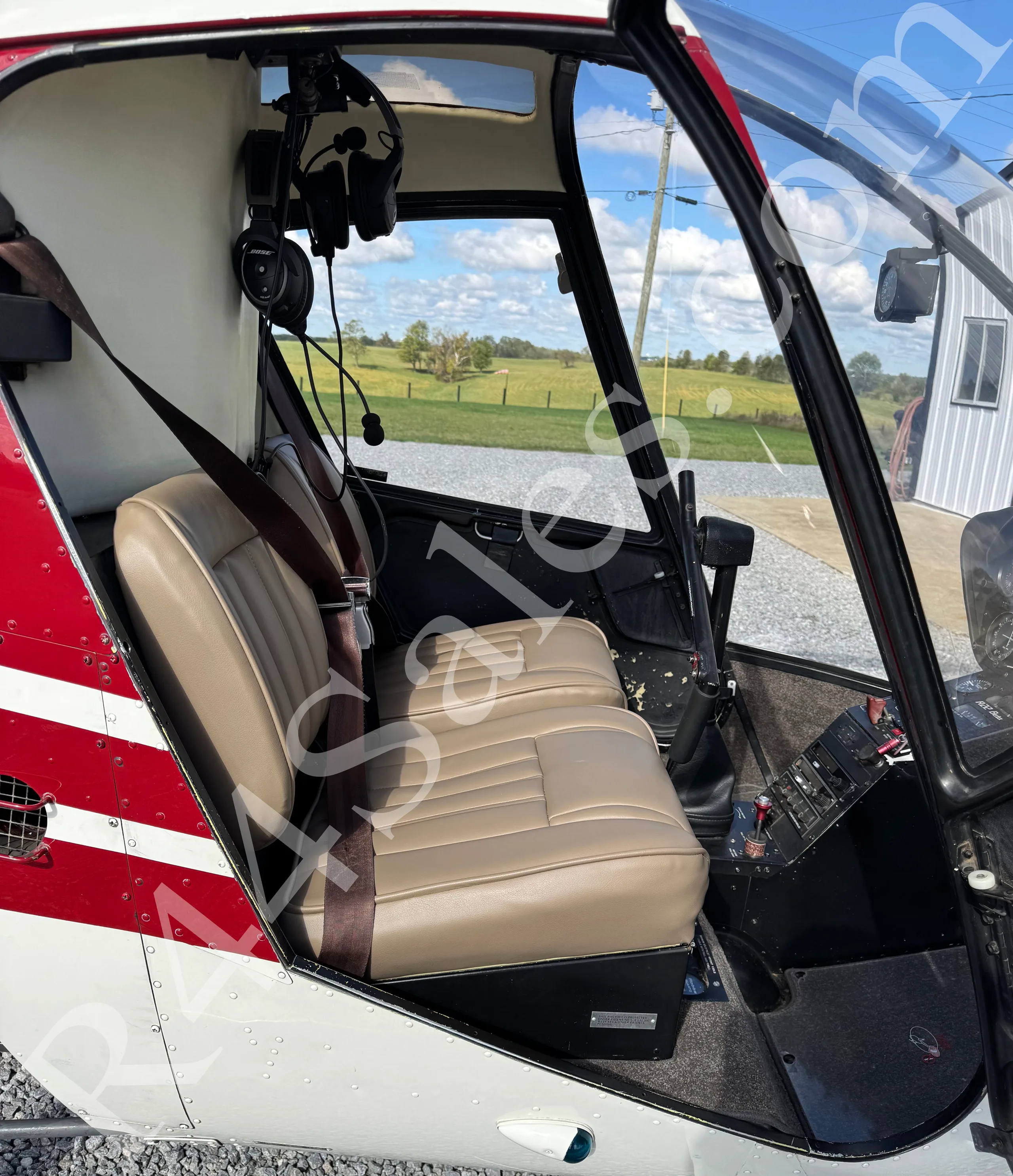 The tan leather seats of a Robinson R22 helicopter cabin with a headset hanging above.