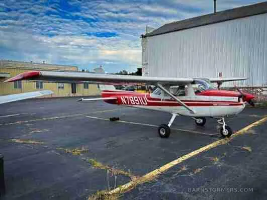 A red and white Cessna N7891U aircraft is parked on an asphalt tarmac next to a white hangar under a cloudy sky.