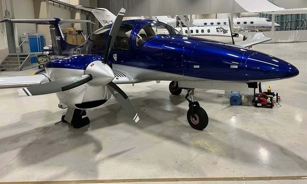 A blue and silver Diamond DA62 twin-engine aircraft is parked in a hangar.