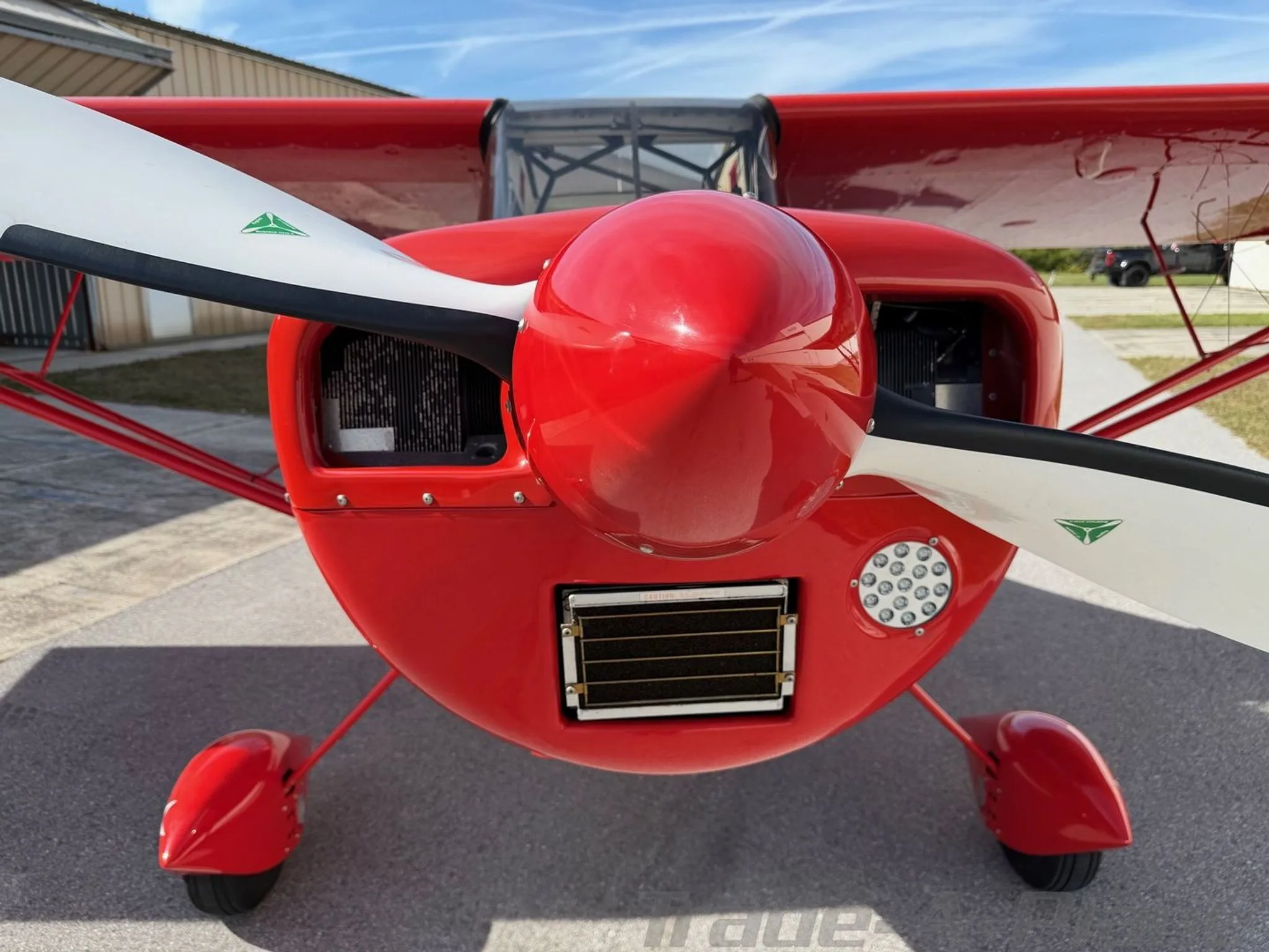 A close-up front view of the red American Champion Xtreme Decathlon aircraft, showing its propeller, cowling, and landing gear.