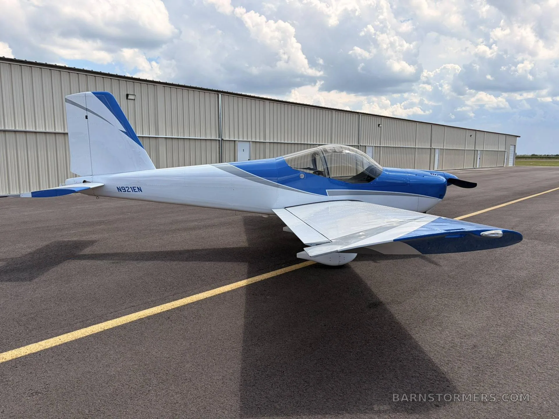A blue and white single-engine aircraft with registration N921EN, viewed from the side, parked on an asphalt tarmac.