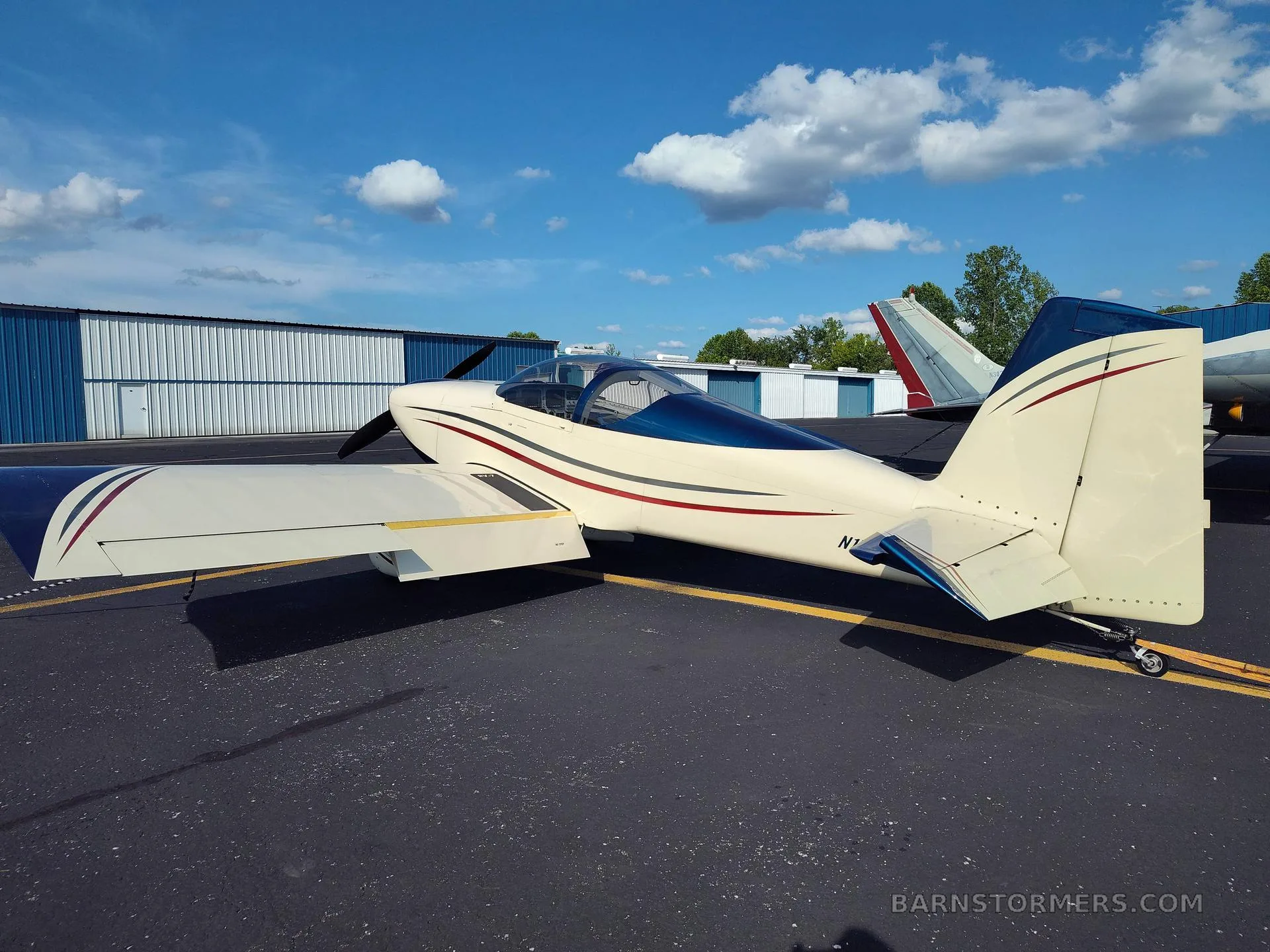 A cream and blue single-engine aircraft with red and grey stripes, viewed from the rear-right, parked on an asphalt tarmac.