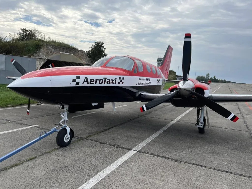 A red, white, and black AeroTaxi Cessna 421 C Golden Eagle III twin-engine aircraft is parked on an airport tarmac with a tow bar attached.