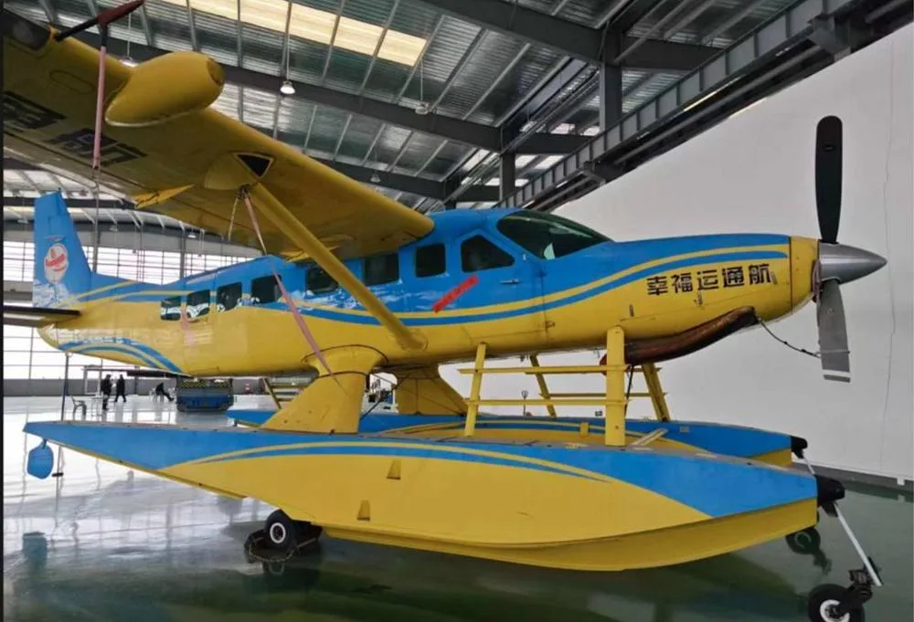 A yellow and blue Cessna Caravan seaplane with Chinese text on the fuselage, viewed from the front-right in a hangar.