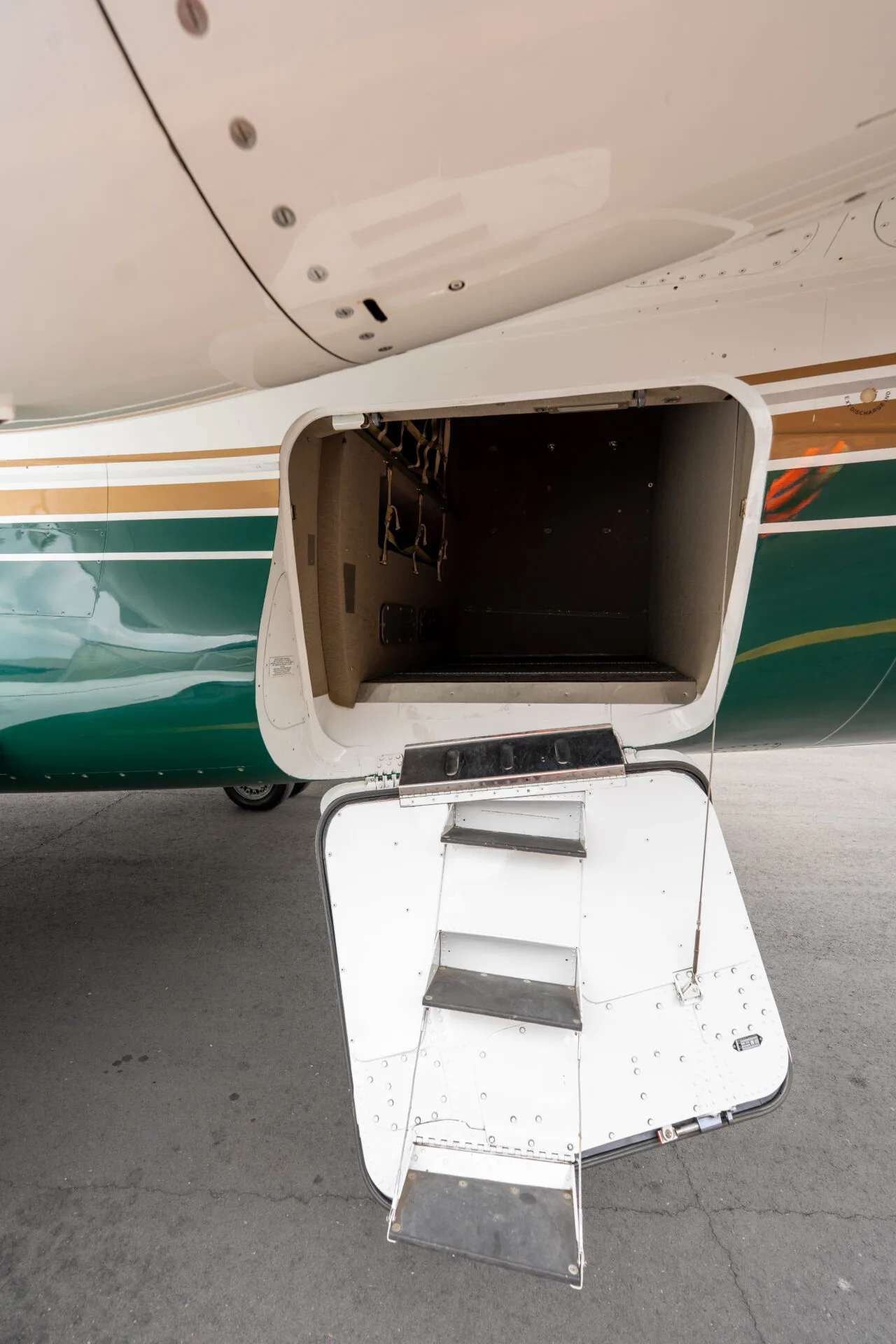 A close-up of the open rear cargo door of a white and green private jet with integrated stairs.