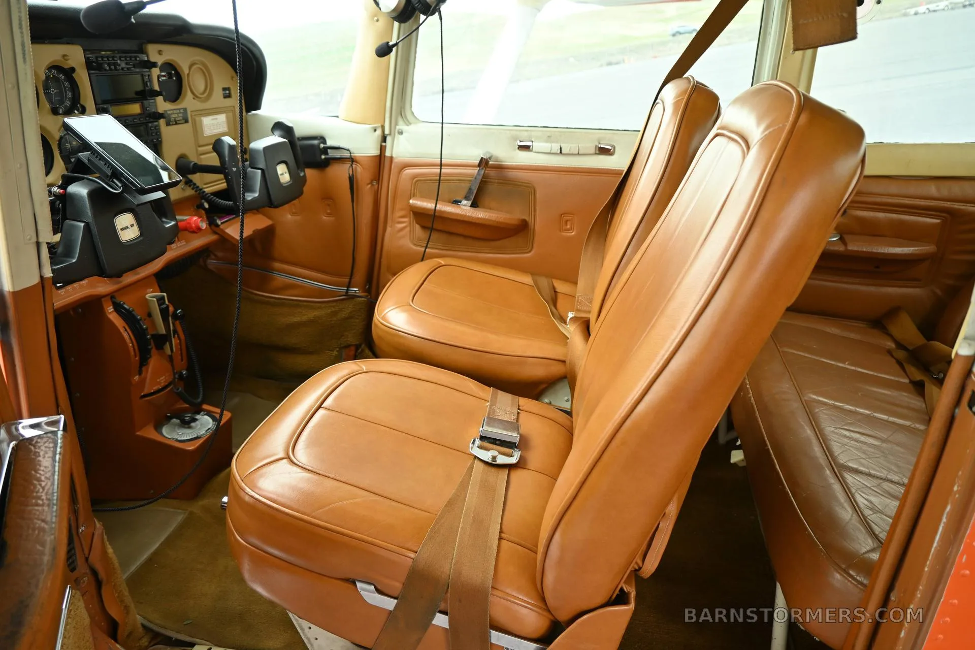 The tan leather interior cabin of a small aircraft, showing two front seats and part of the instrument panel.