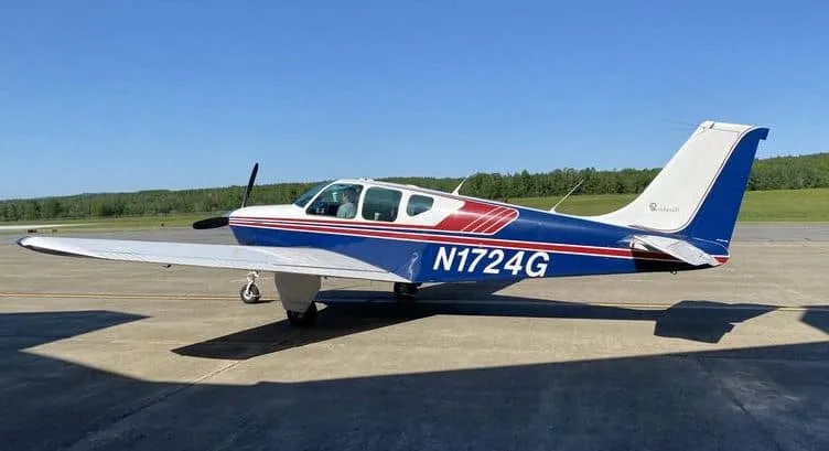 A blue and white single-engine propeller aircraft with red stripes, registration N1724G, parked on an airfield under a clear blue sky.
