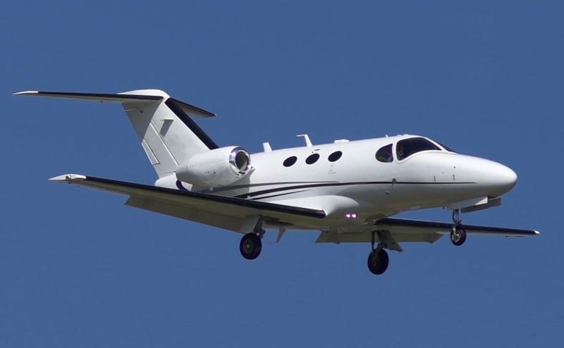 A white Cessna Citation Mustang aircraft in flight against a blue sky.