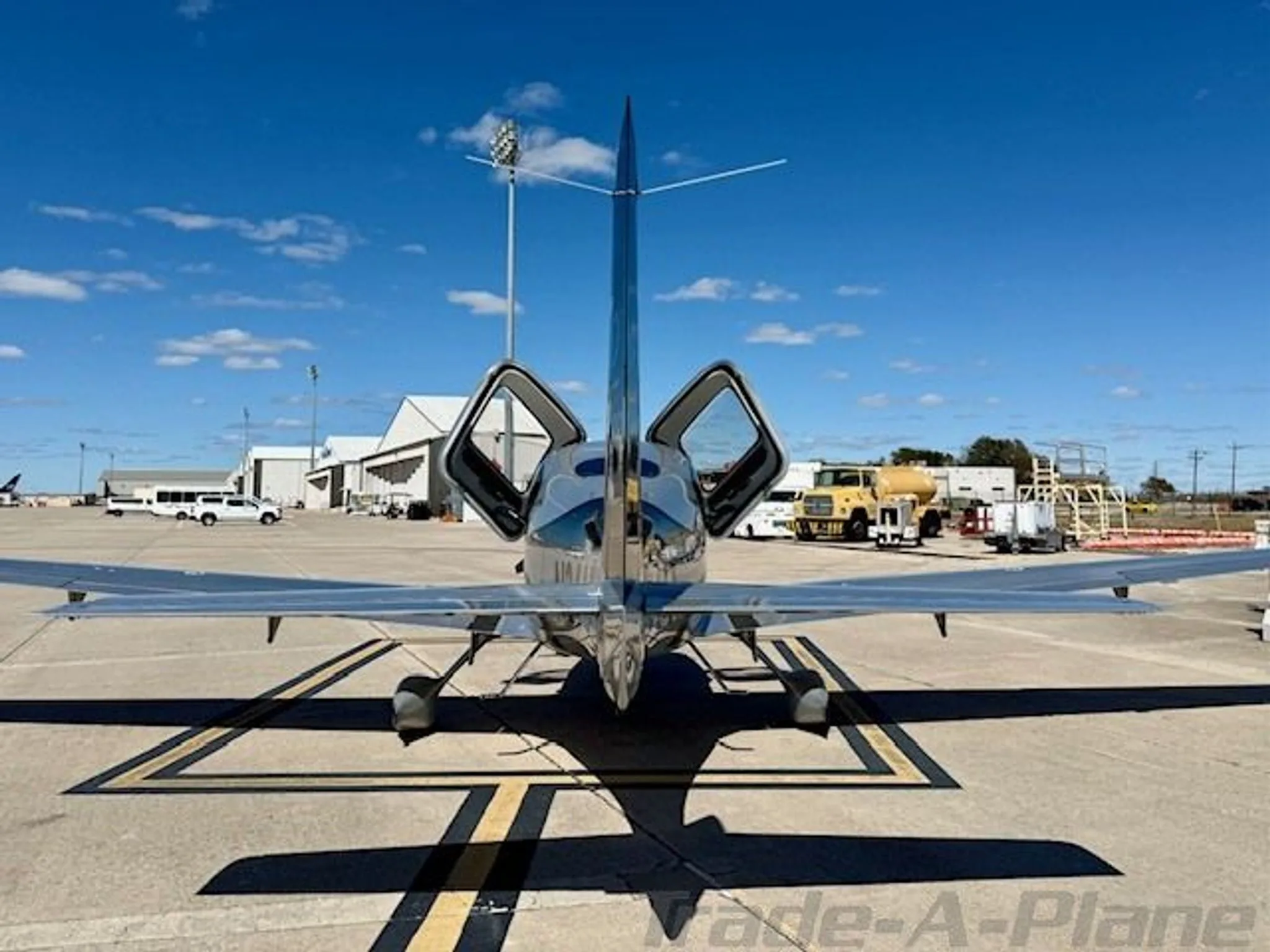 A rear view of a black and silver Cirrus SR22 GTS Turbo aircraft with open doors parked on a tarmac.