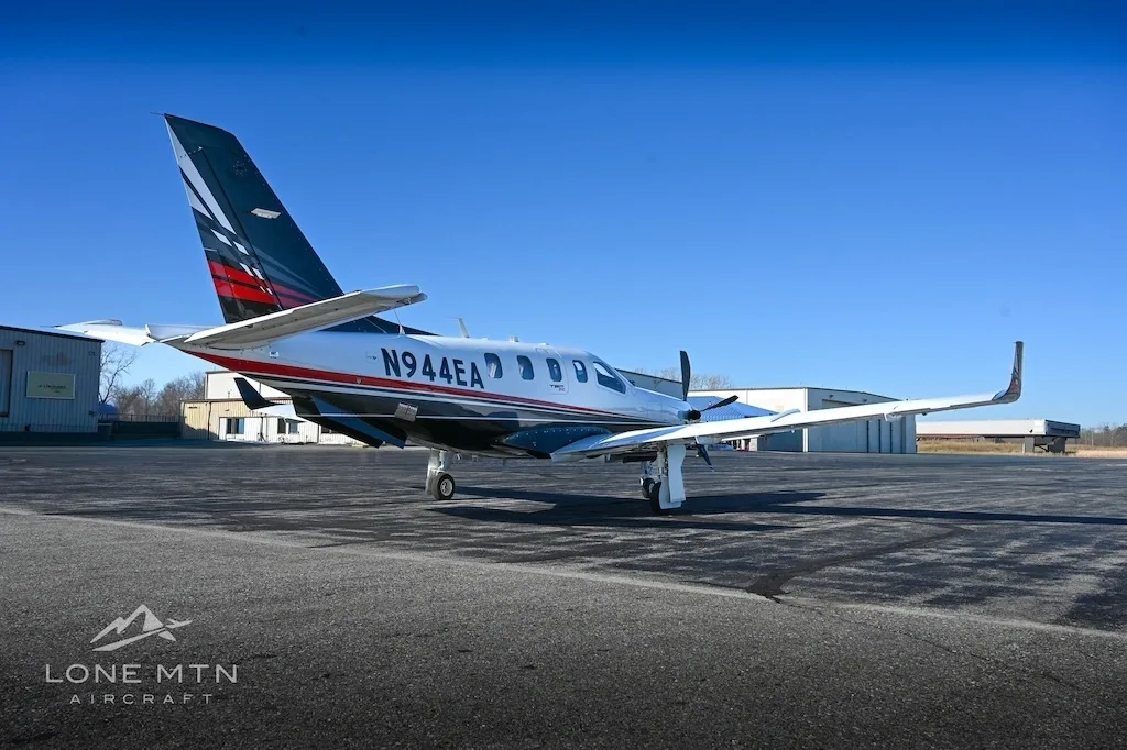A TBM 940 aircraft, registration N944EA, parked on an asphalt ramp with buildings in the background.