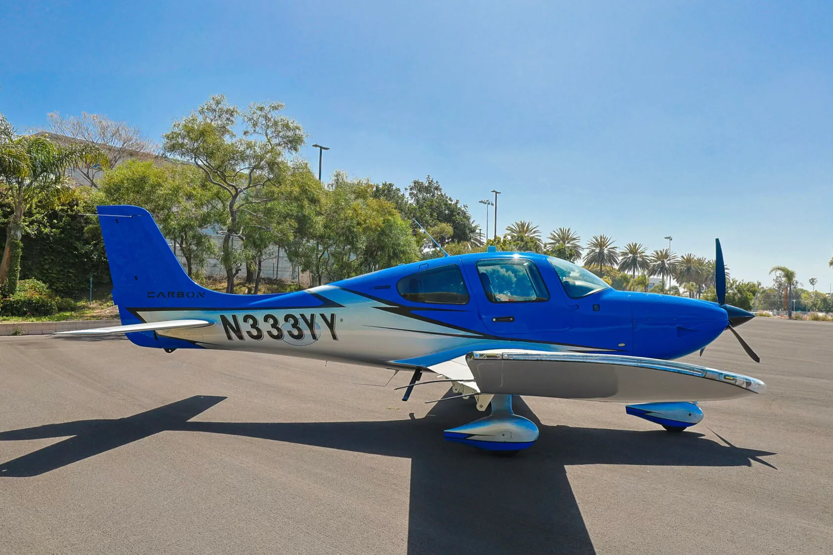 A blue and silver Cirrus SR20 aircraft with tail number N333YY parked on an asphalt ramp under a clear blue sky.