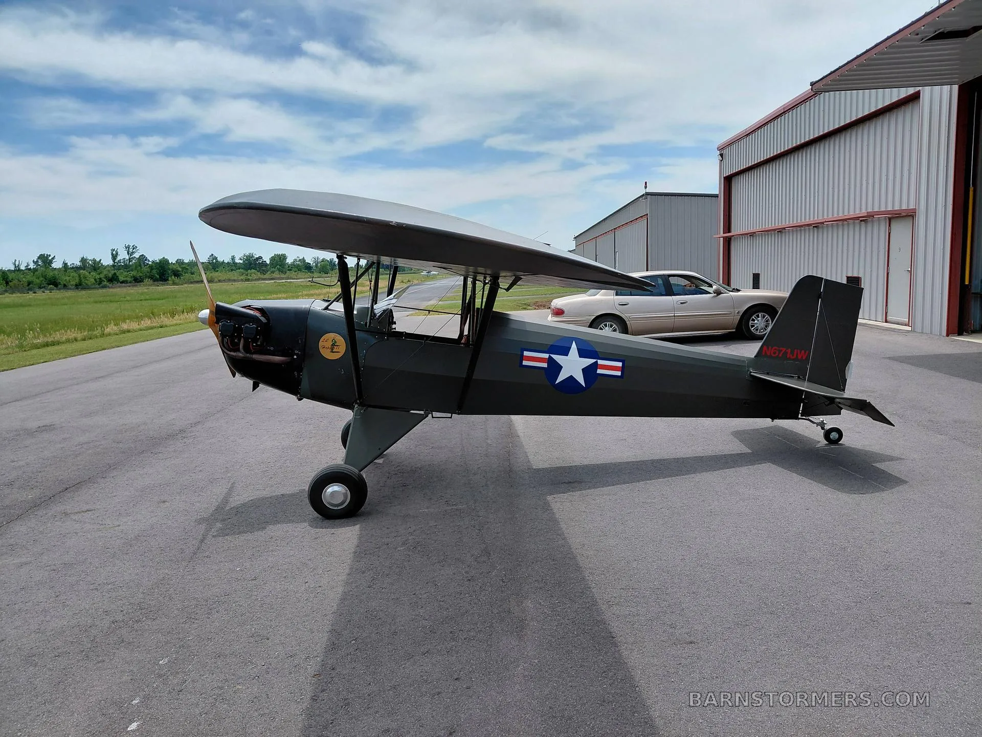 A dark green single-engine, high-wing aircraft with a US Army star insignia on its side, parked on an asphalt apron next to a hangar.