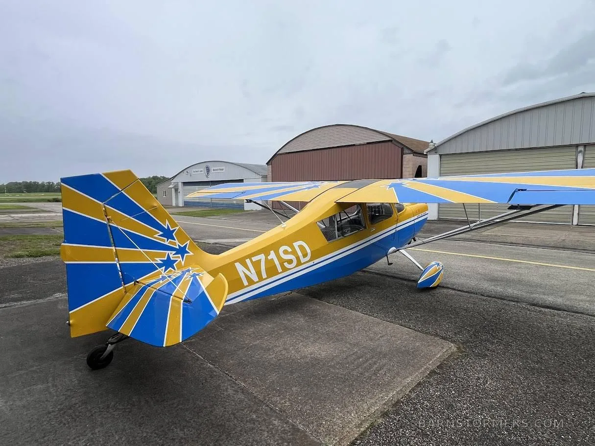 A yellow and blue Super Decathlon aircraft with tail number N71SD parked on an apron, viewed from the rear-right.