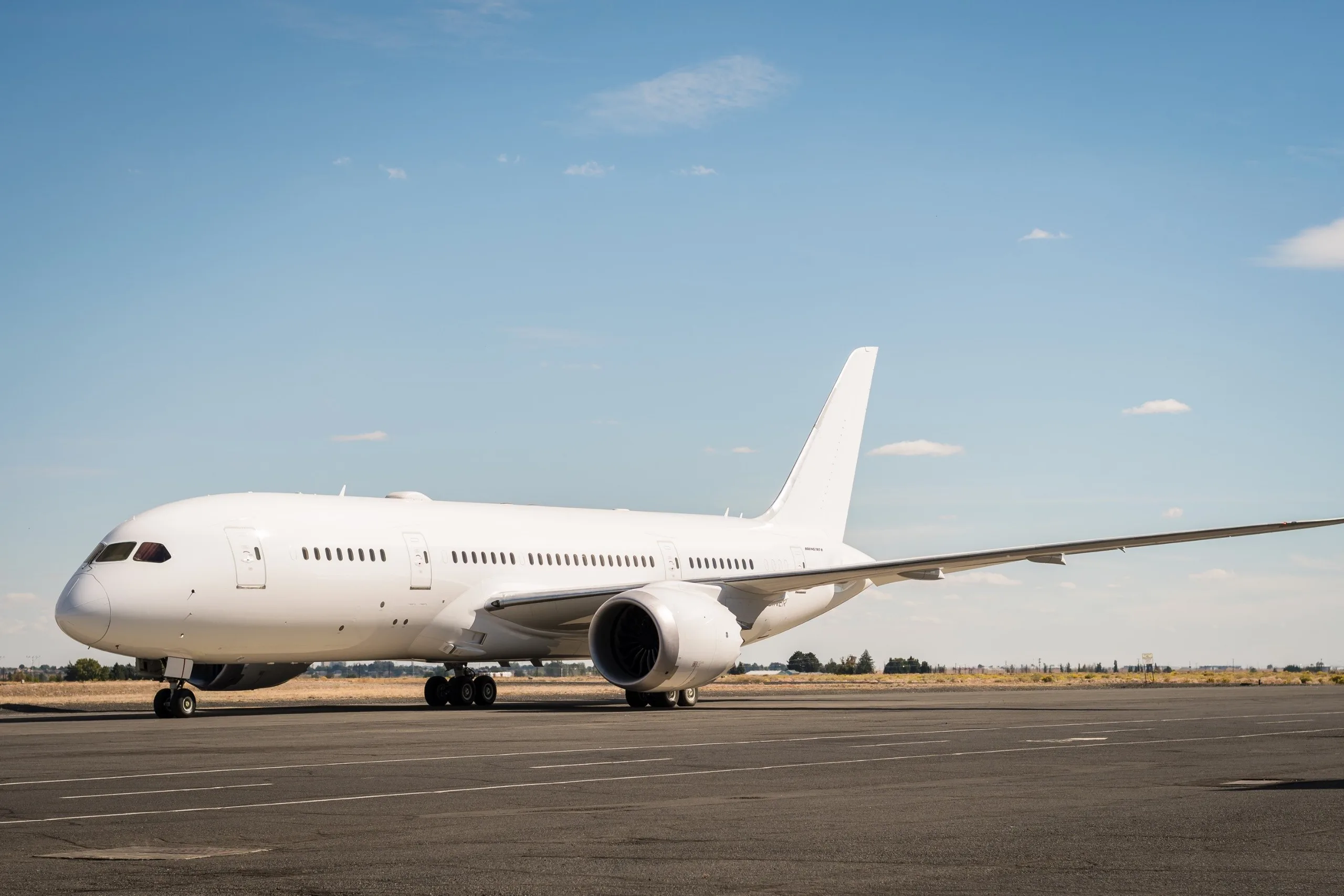 A white Boeing 787 Dreamliner aircraft parked on an airfield under a clear blue sky.