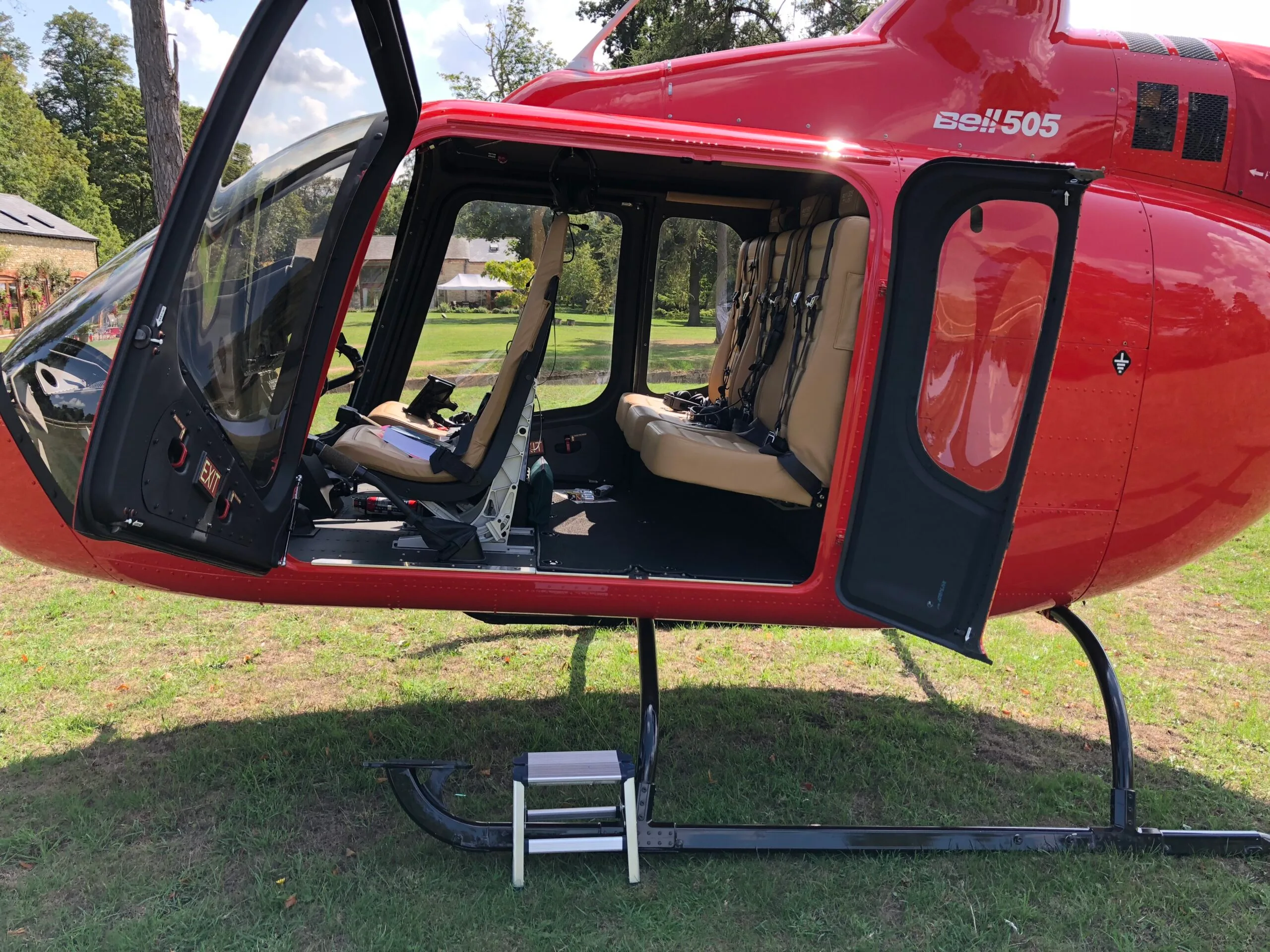 The open cabin of a red Bell 505 helicopter reveals tan leather seats and a small step stool on the skid.