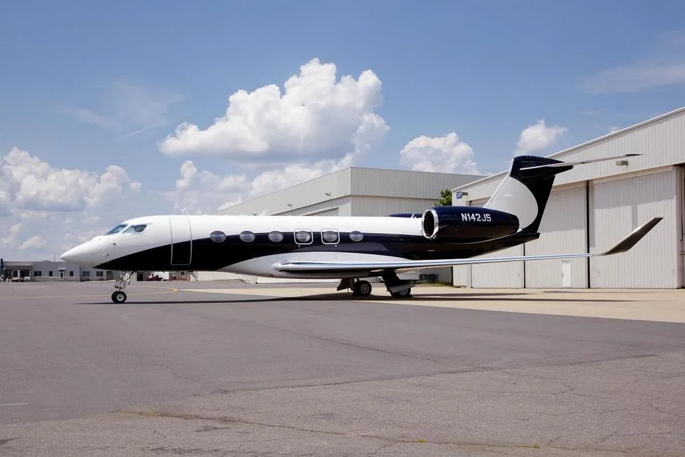 A white and black Gulfstream G600/G650 business jet, registration N142JS, parked on an airfield.