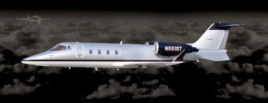 A Learjet N551ST in flight against a dark, cloudy, artificial background.