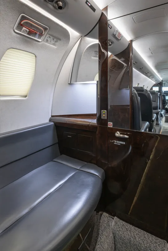 The aircraft cabin interior, featuring a side bench seat, wood paneling, and a view towards the rear.
