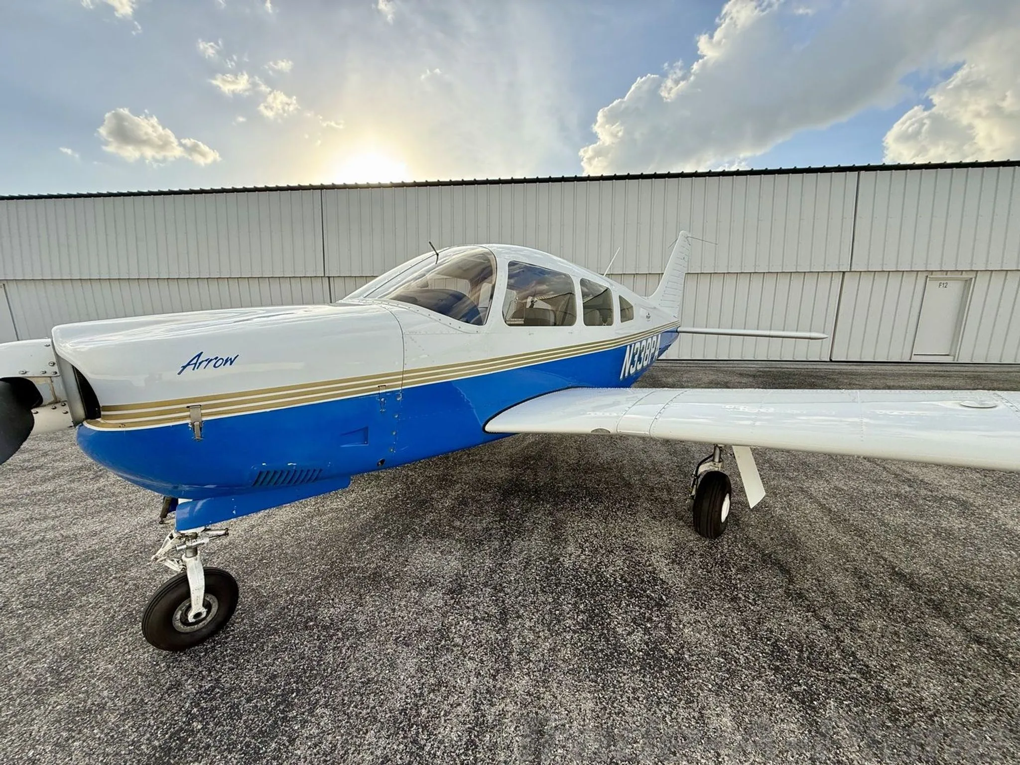 A close-up front-side view of the white and blue Piper Arrow aircraft (N338PA) on the tarmac with the sun setting.