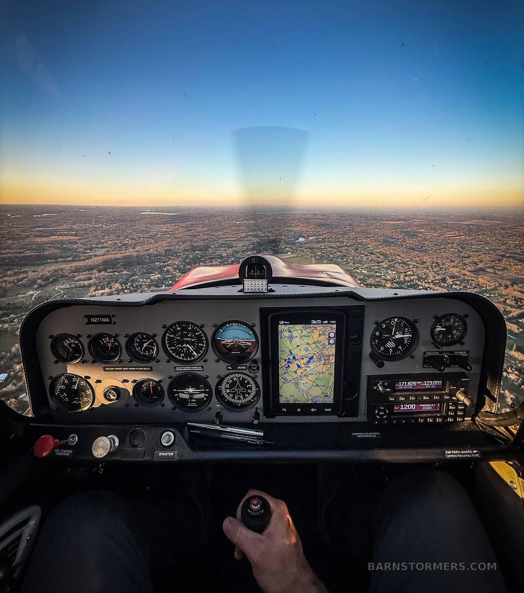 A pilot's view from the cockpit showing the instrument panel and a vast landscape under a clear sky at sunset.