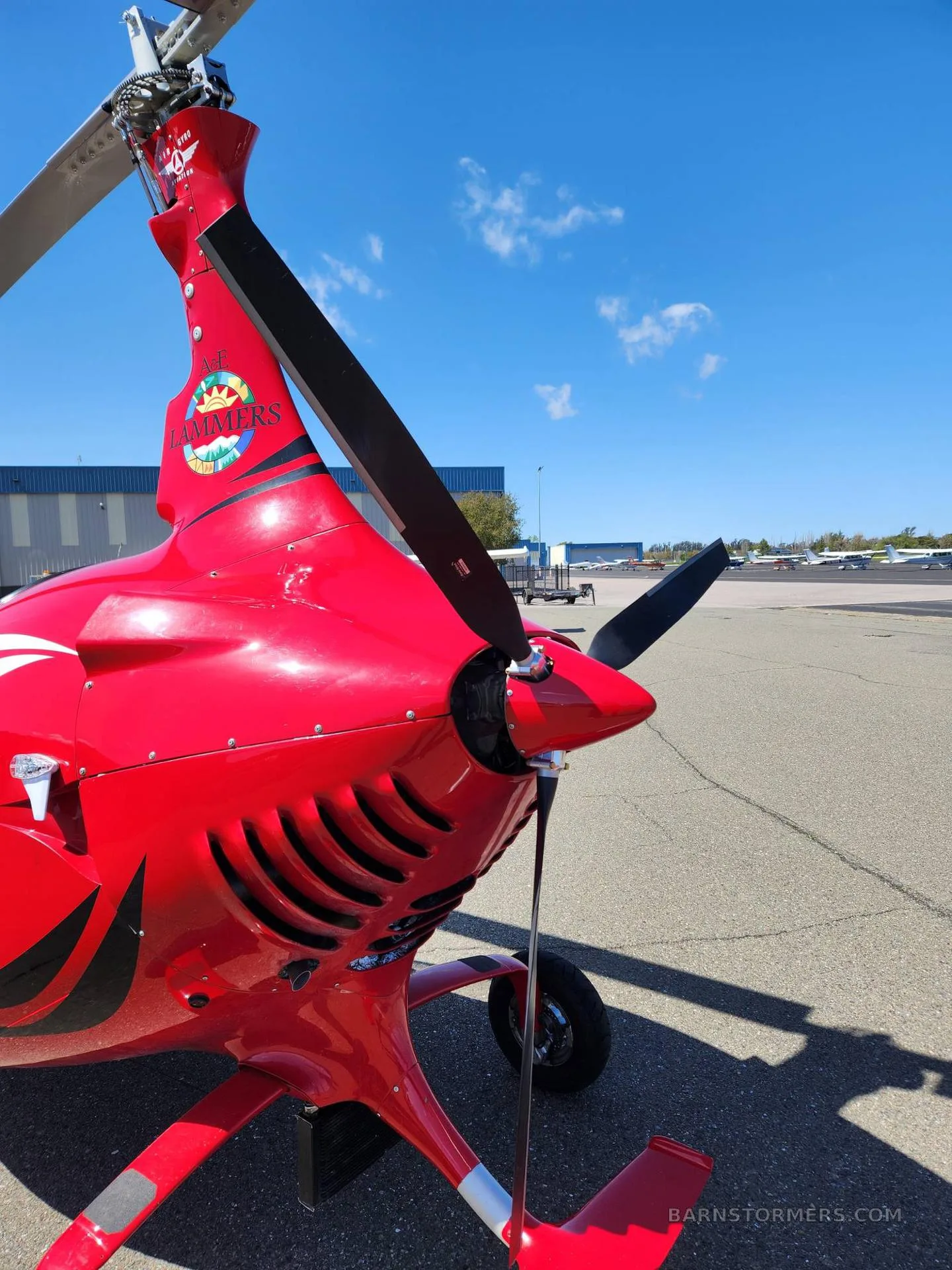 A close-up view of the red gyrocopter's tail section and propeller, with a 'ME LANDERS' logo on the tail.