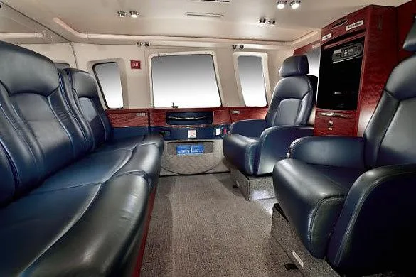 A spacious aircraft cabin features dark blue leather seating, a wooden cabinet, and large windows.