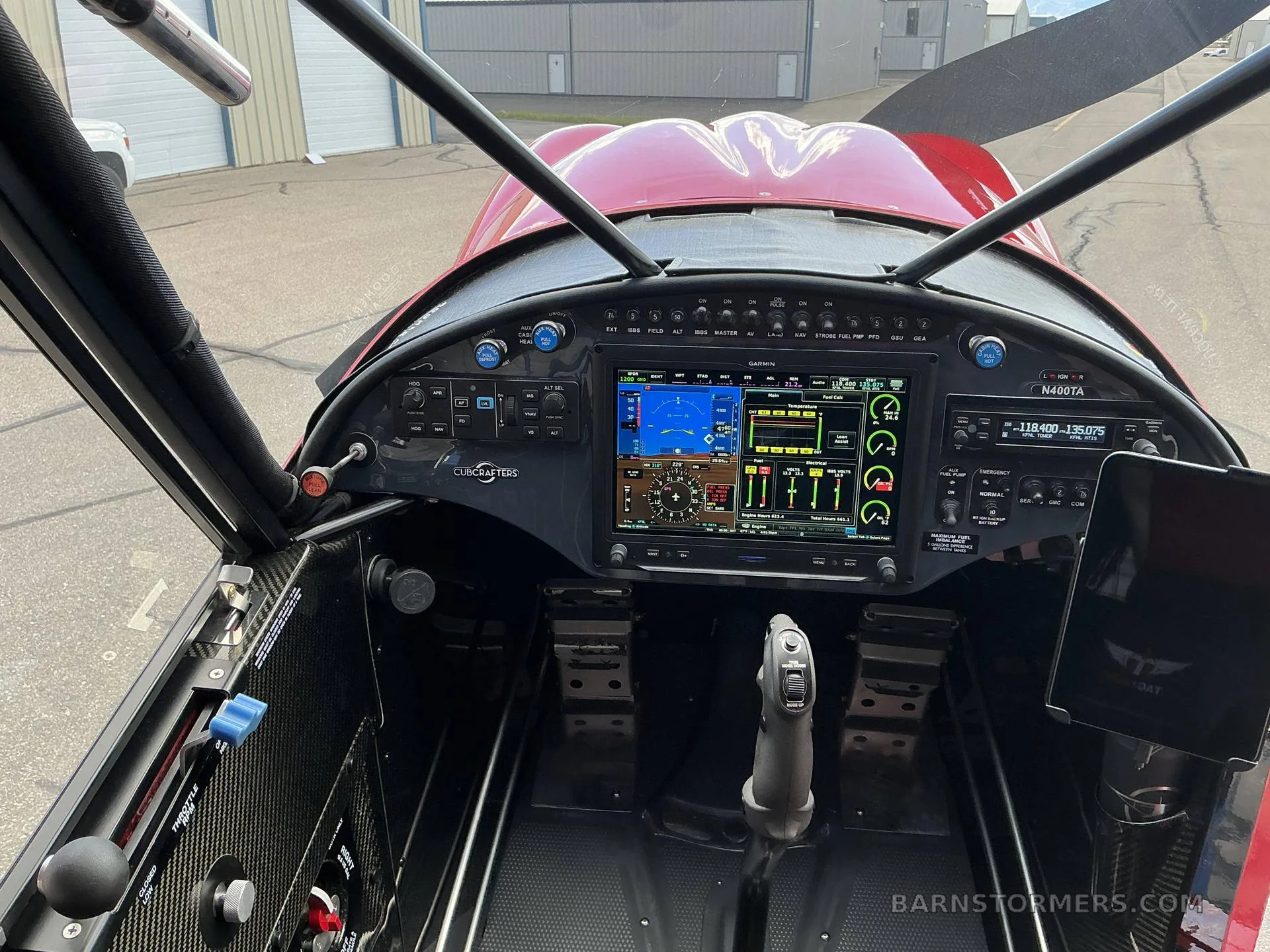 The cockpit of a red aircraft, showing a modern glass panel with a large Garmin display and flight controls.