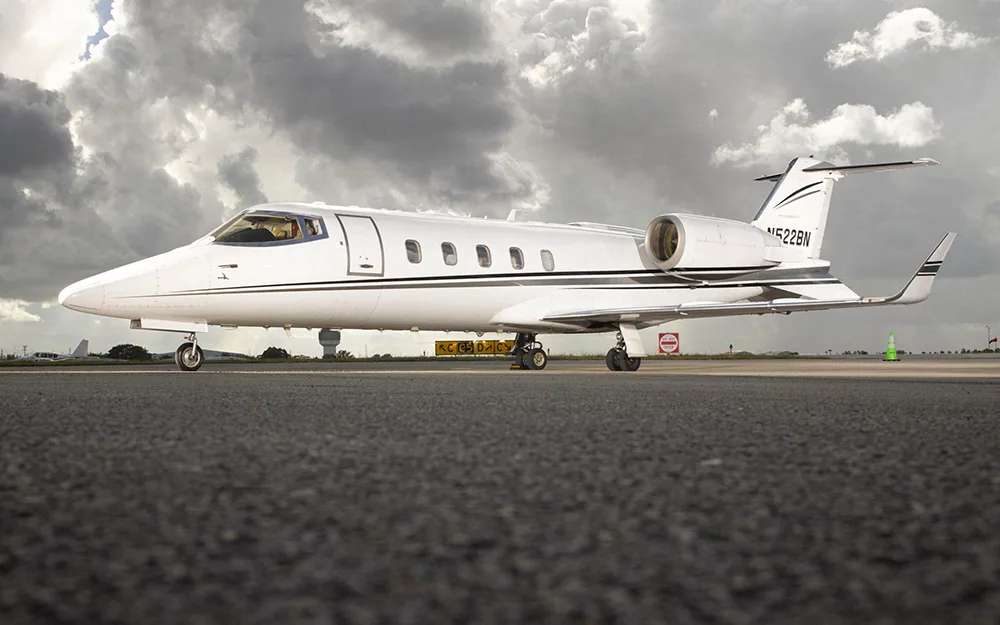 A white Learjet with black and grey stripes, tail number N522BN, parked on a tarmac under a cloudy sky.