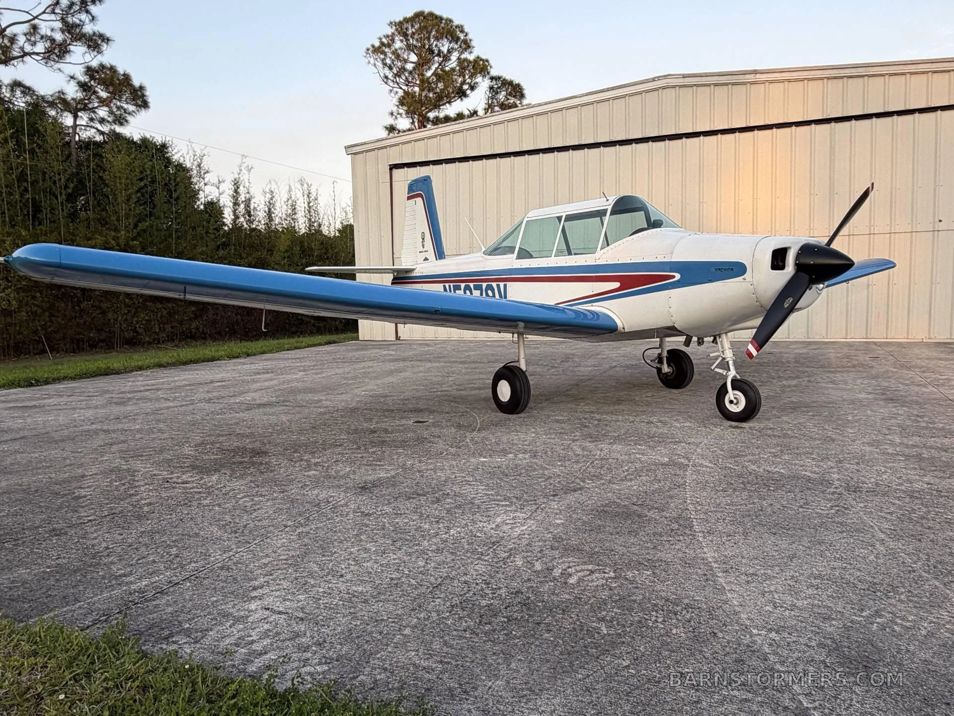 A white and blue single-engine aircraft with registration N5078V, parked on a concrete pad in front of a hangar, viewed from the front-left.