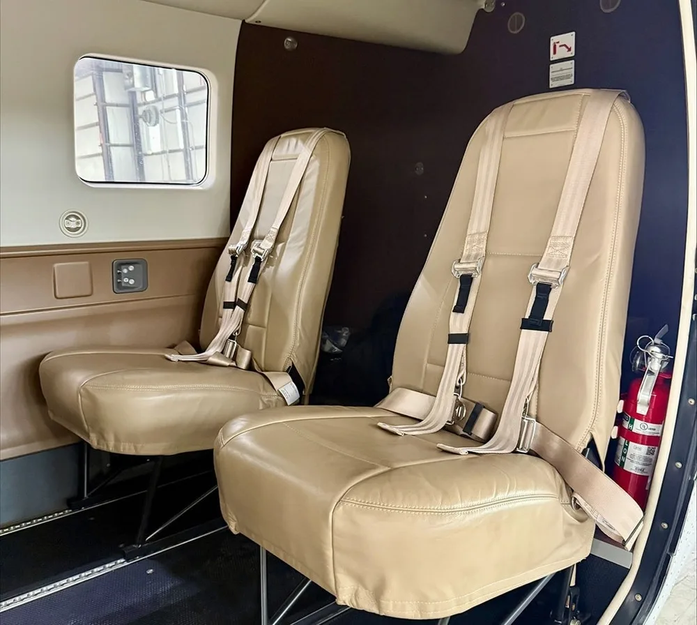 Two tan leather passenger seats with harnesses and a fire extinguisher in the aircraft cabin.