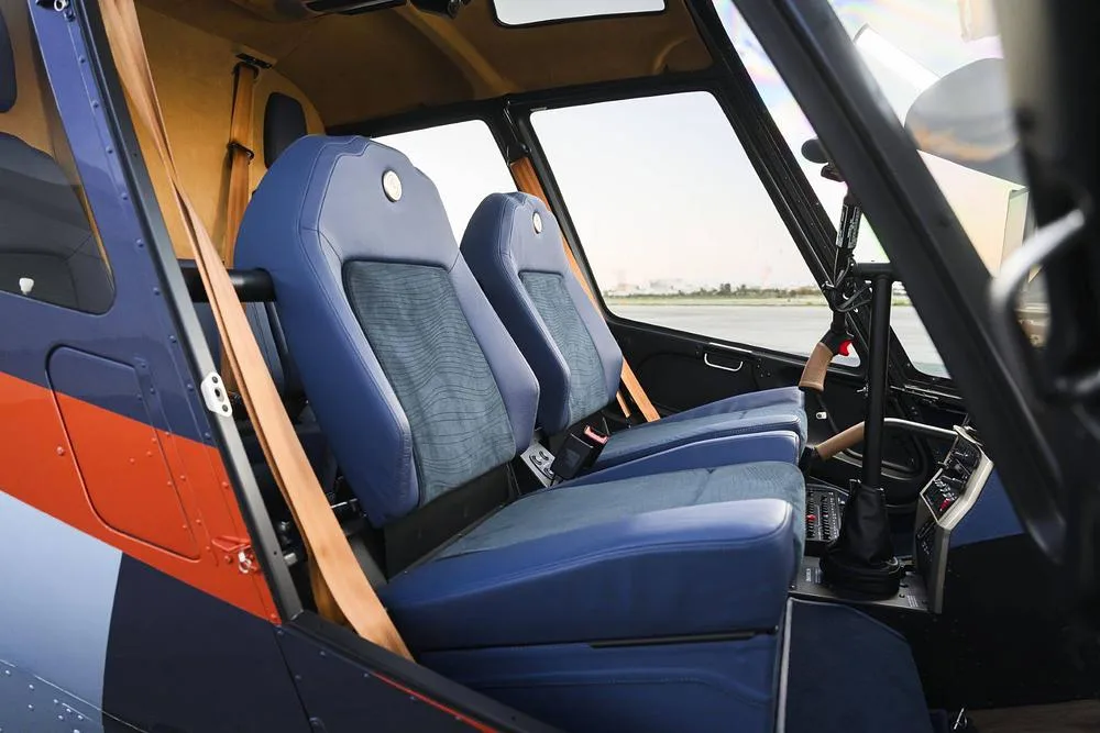 The front blue seats of a helicopter cabin with a view of the outside through the large windows.