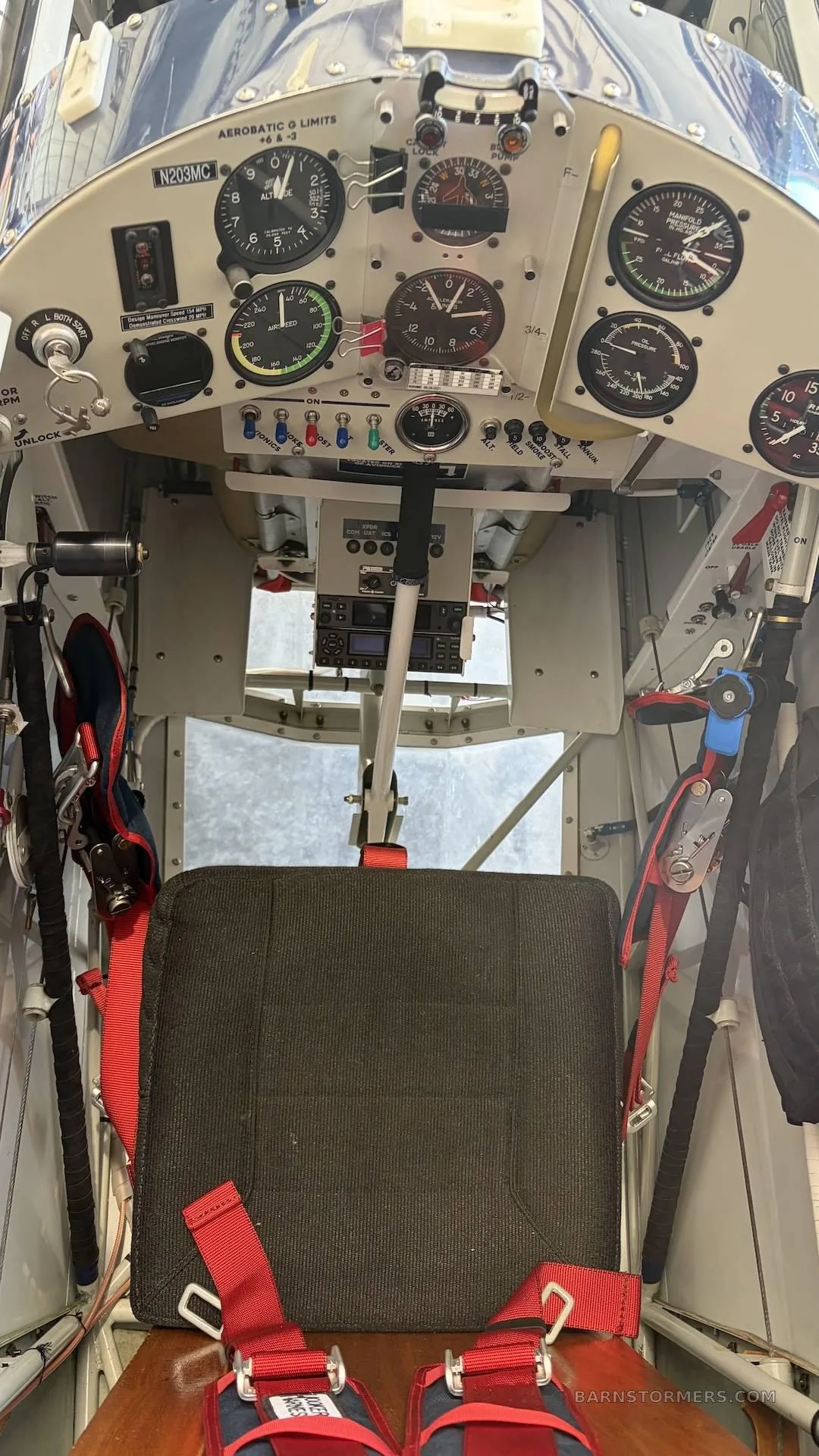 The cockpit of a biplane features a dark seat, red harnesses, and a white instrument panel with gauges.