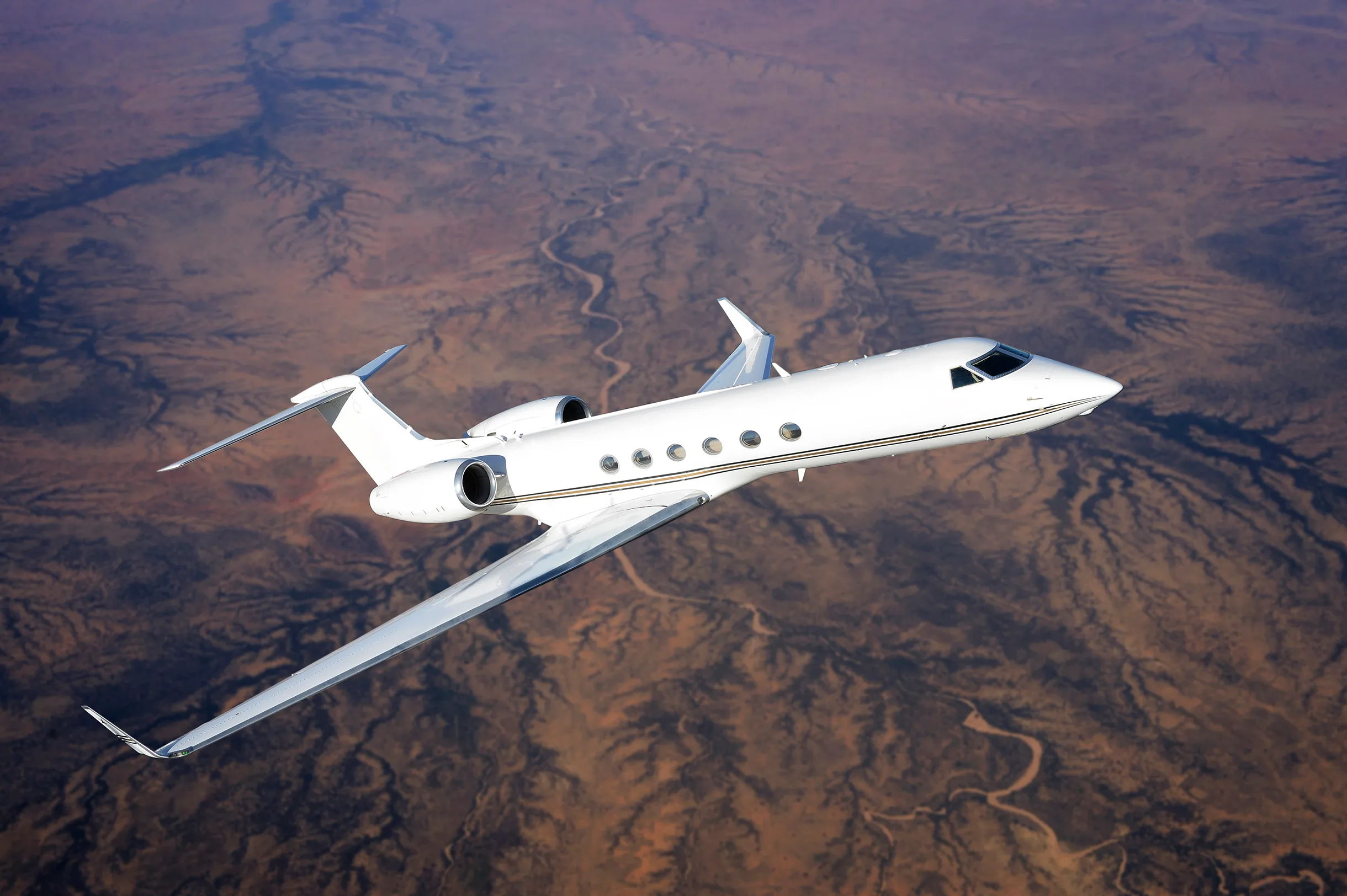 A white Gulfstream business jet flying over a desert landscape.