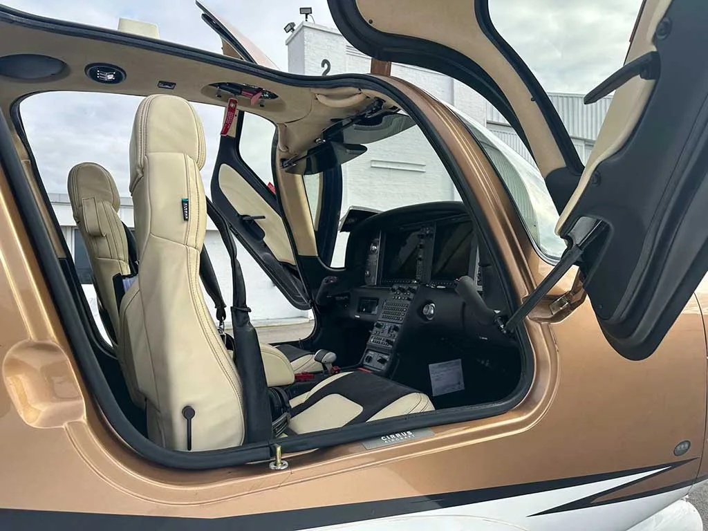 The open cabin of a Cirrus SR22 aircraft, showing the beige and black seats and part of the cockpit.