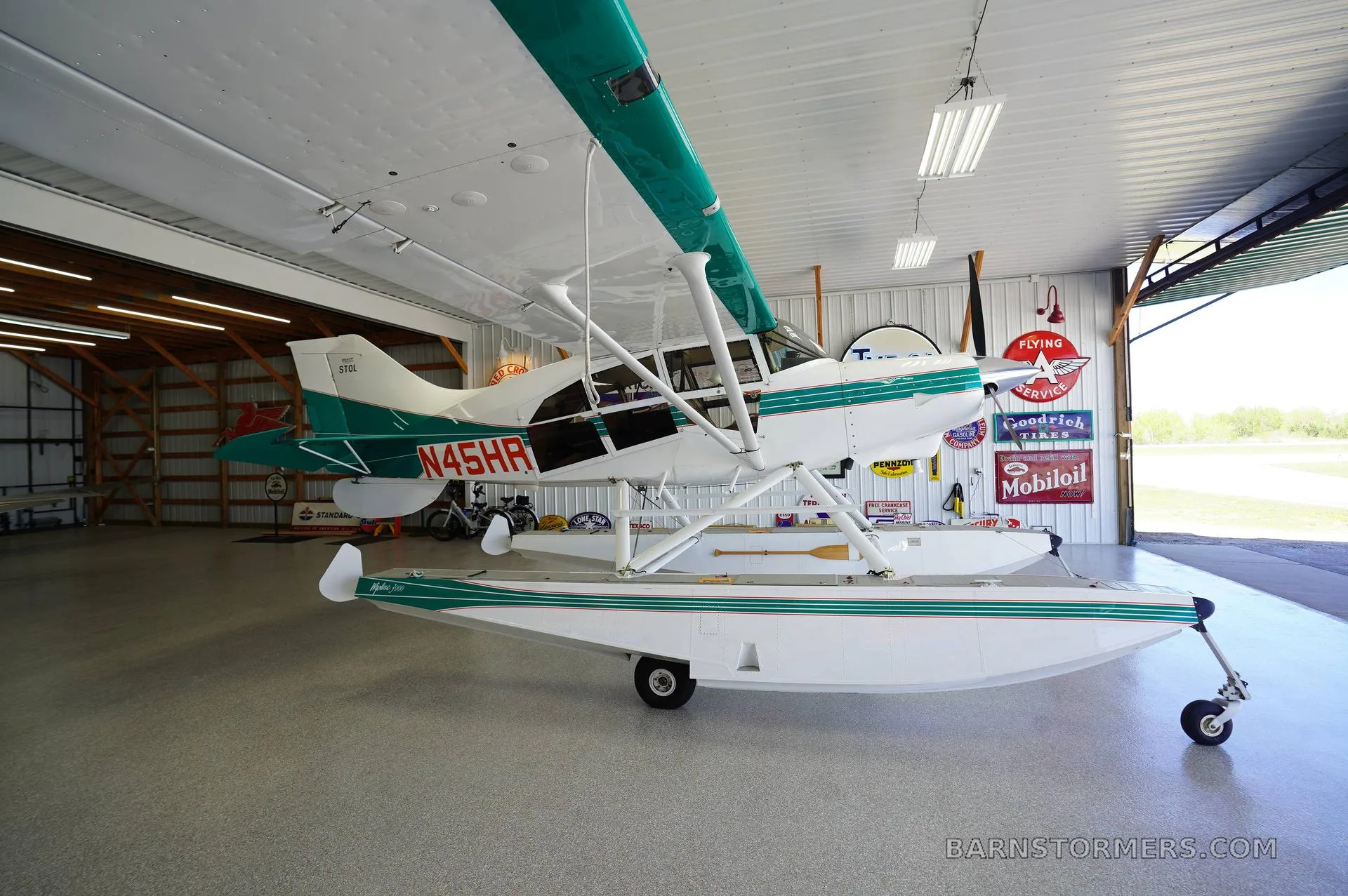A white and teal floatplane, registration N45HR, is parked inside a hangar, viewed from the front-left.