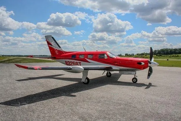 A red and white Piper M600 SLS aircraft with registration N325ST is parked on an asphalt ramp under a partly cloudy sky, viewed from the left side.
