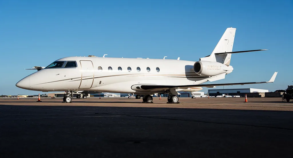 A side view of a white Gulfstream G280 business jet with gold and black stripes, registration N280LT, parked on an airport tarmac.
